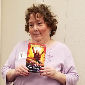Picture of Ronda Del Boccio holding her paranormal/urban fantasy novel They All Died Smiling